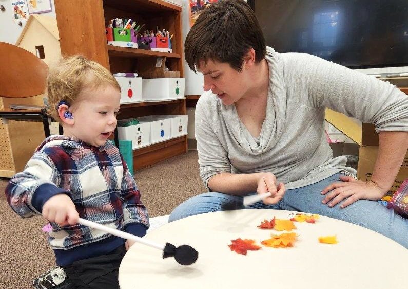 teacher and child with hearing aid banging a big drum