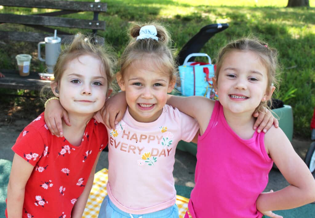 three girls with their arms around one another's shoulders wearing pink and red